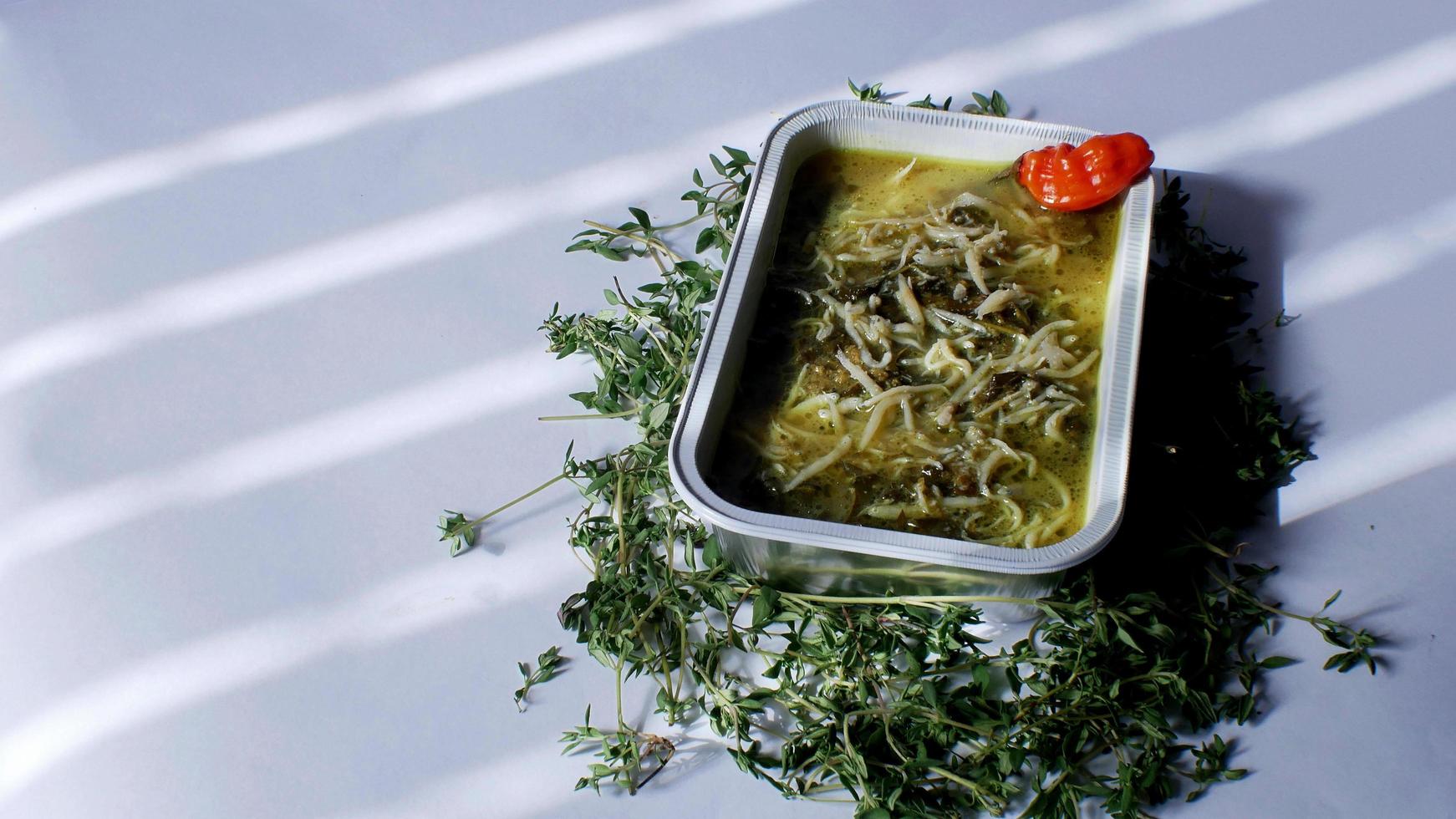 vegetal de folha de mandioca com anchovas comida indonésia servida em um recipiente de alumínio com fundo branco foto