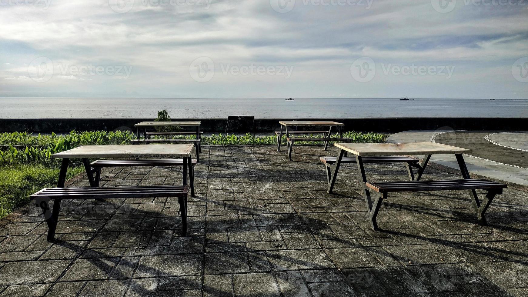 fileiras de cadeiras e mesas minimalistas para relaxar curtindo a praia em anjungan vovasanggayu na regência de pasangkayu, indonésia com fundo do mar foto