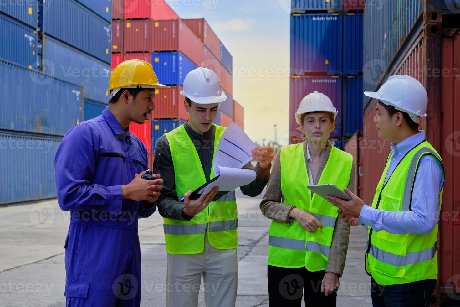 um grupo de trabalhadores multirraciais em uniformes de segurança e capacetes trabalham no terminal logístico com muitas pilhas de contêineres, carregando mercadorias de transporte de controle para o setor de transporte de carga. foto