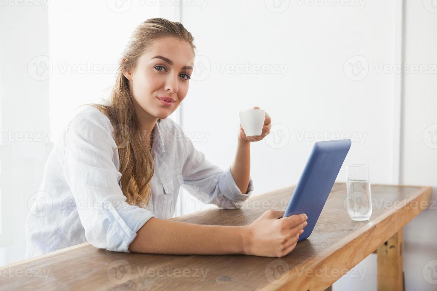 loira bonita tomando café enquanto estiver usando tablet foto