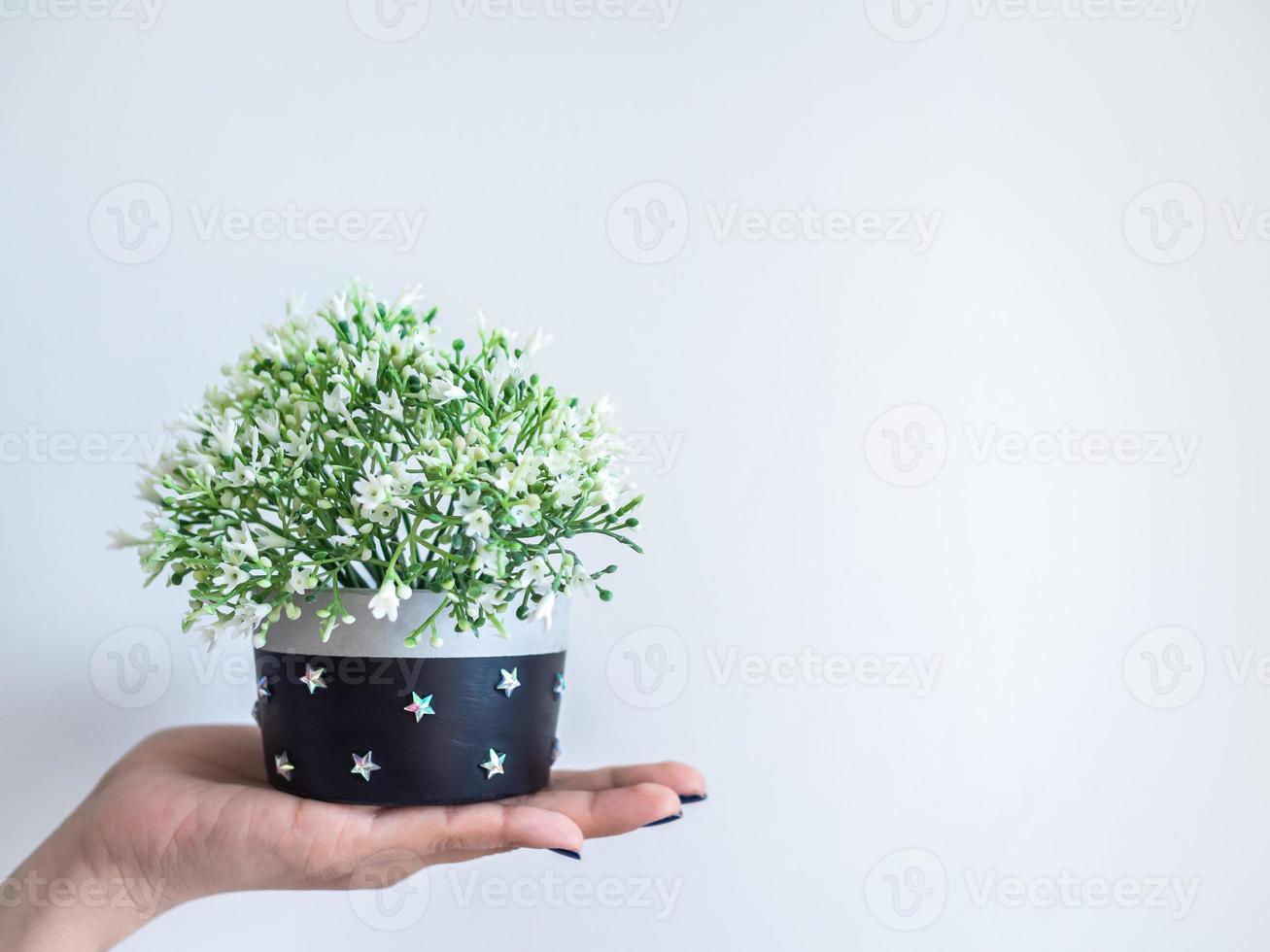 mão mostrando plantador de concreto redondo moderno preto com flor branca. vaso de concreto pintado para decoração de casa foto