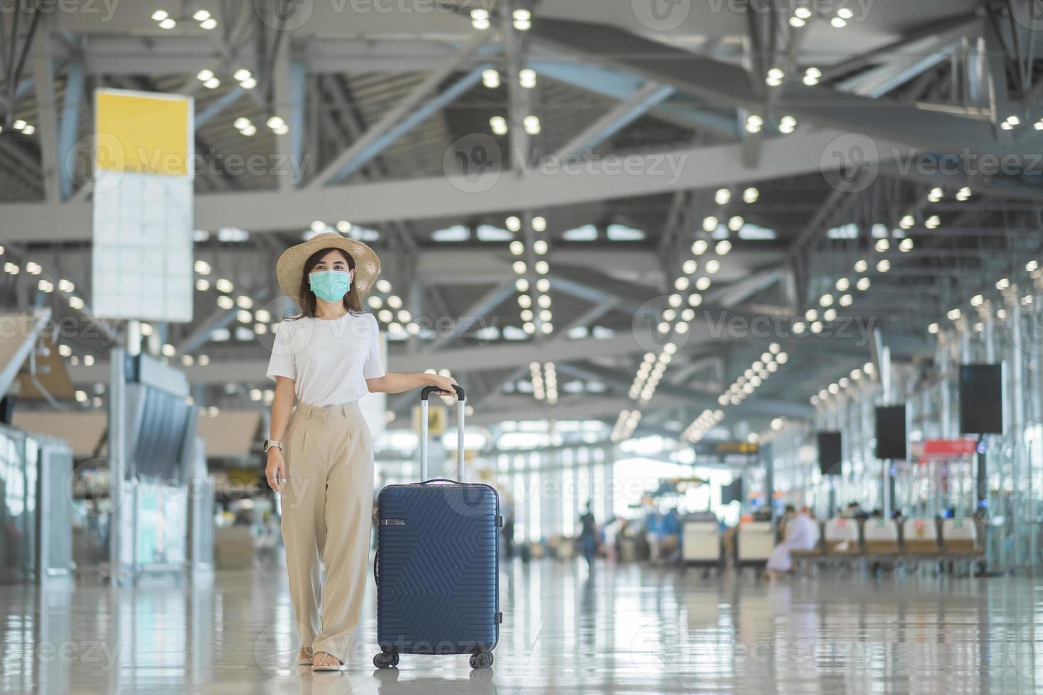 jovem mulher usando máscara facial com bagagem andando no aeroporto, proteção contra infecção por doença de coronavírus, viajante asiática com chapéu. hora de viajar após o conceito de dose de reforço de vacina foto
