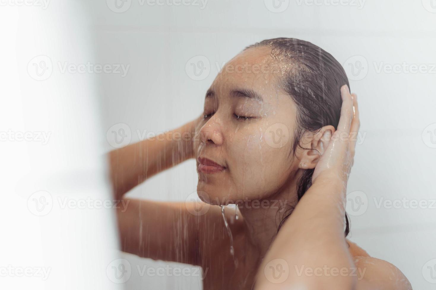 jovem mulher lavando o cabelo no chuveiro. mulher asiática lavando o cabelo preto. foto