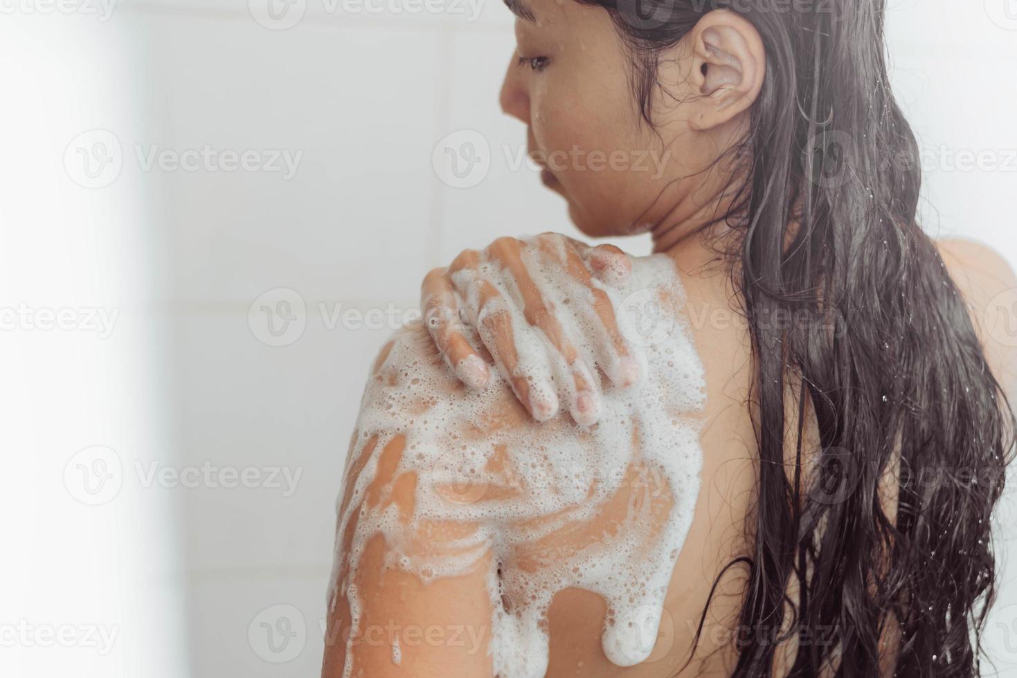 jovem mulher lavando o corpo no chuveiro. mulher asiática tomar banho no banheiro. foto