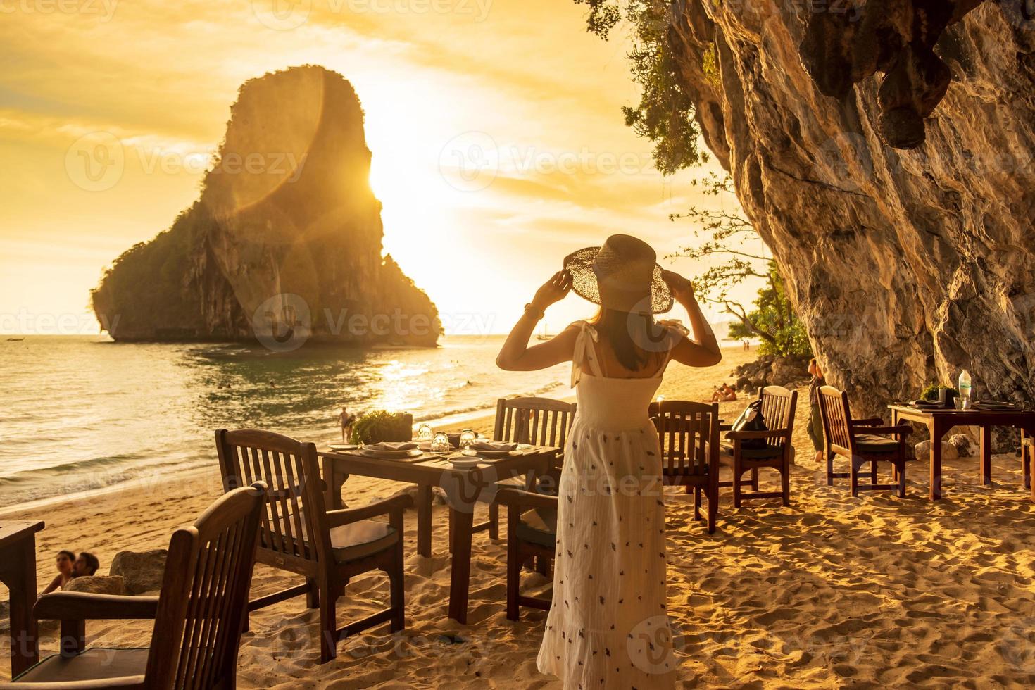turista de mulher em jantar de vestido branco na caverna do restaurante na praia de phra nang ao pôr do sol, railay, krabi, tailândia. férias, viagens, verão, desejo de viajar e conceito de férias foto