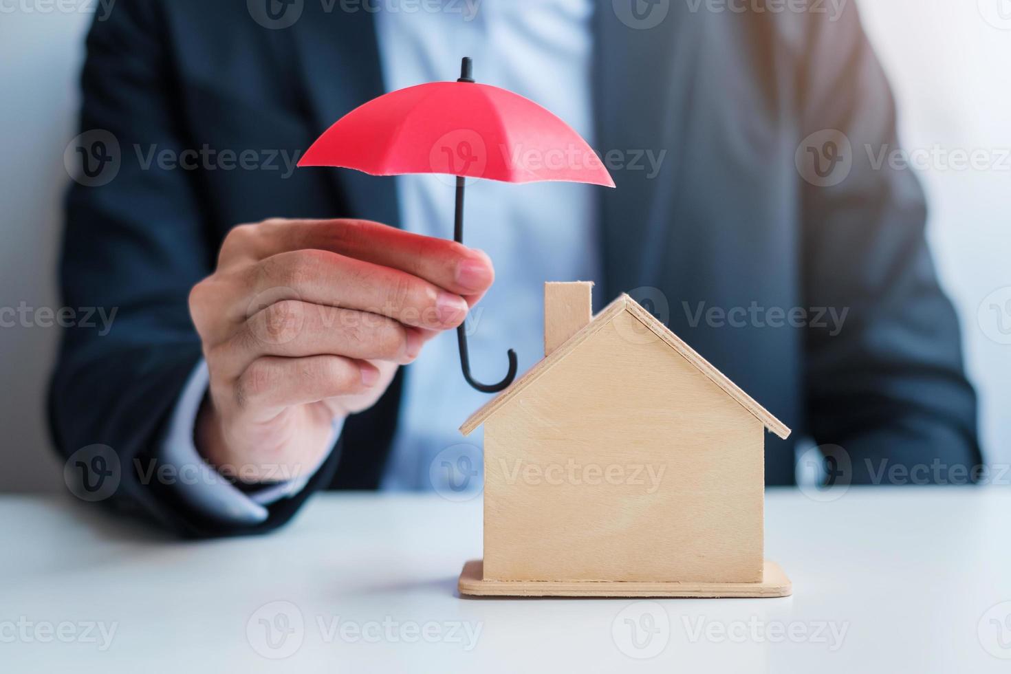 mão de empresário segurando o modelo de casa de madeira da tampa do guarda-chuva vermelho. conceitos imobiliários, seguros e imobiliários foto