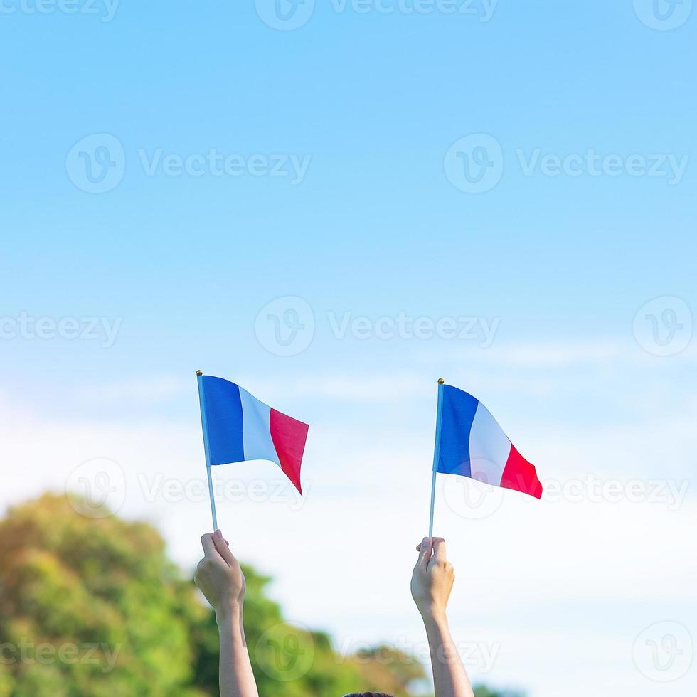 mão segurando a bandeira da frança no fundo do céu azul. feriado do dia nacional francês, dia da bastilha e conceitos de celebração feliz foto