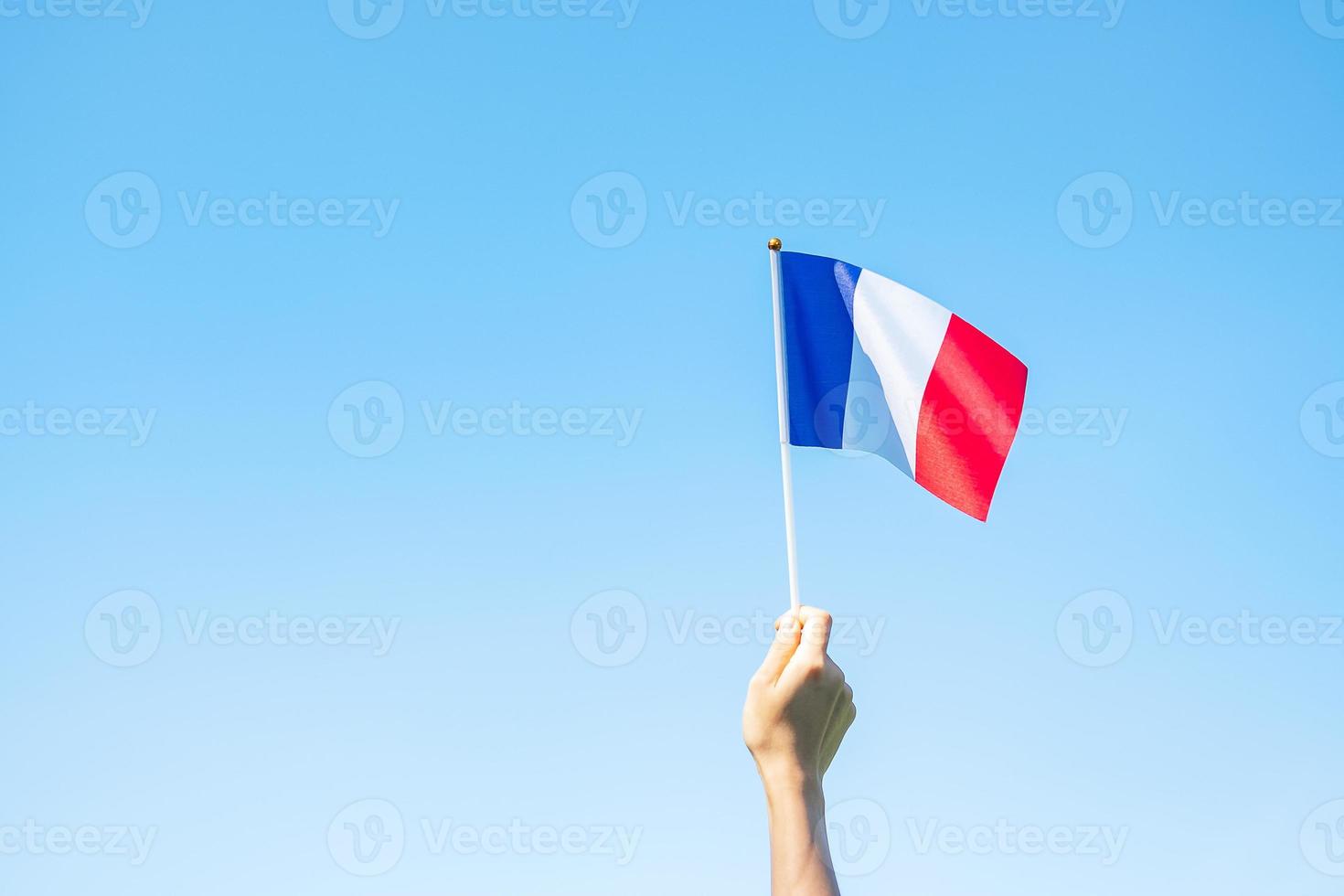 mão segurando a bandeira da frança no fundo do céu azul. feriado do dia nacional francês, dia da bastilha e conceitos de celebração feliz foto