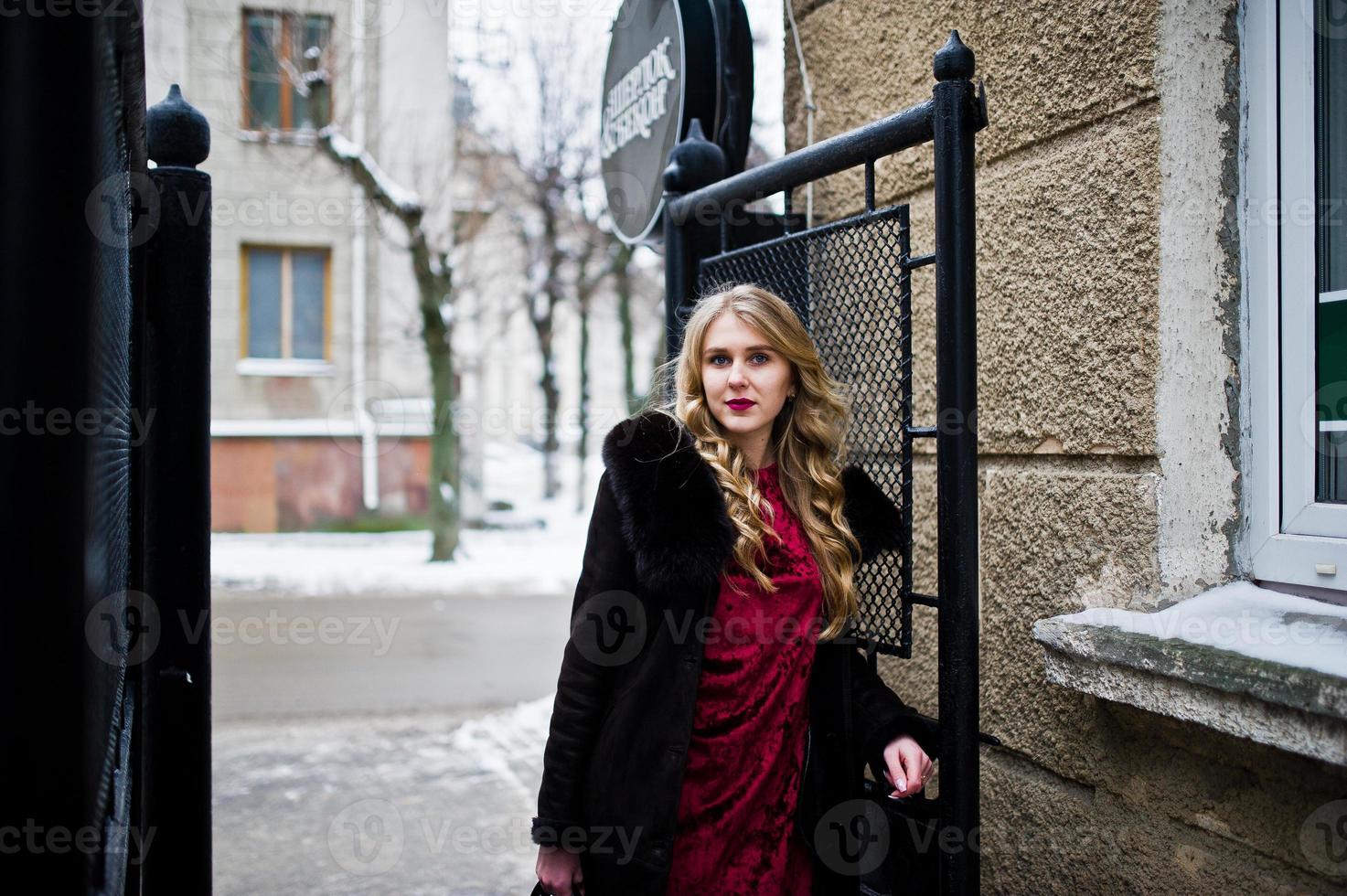 elegância loira em vestido de noite vermelho e casaco de pele nas ruas da cidade em dia de inverno. foto