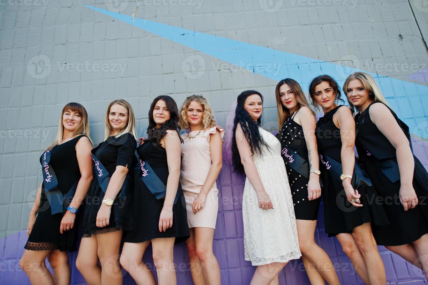 grupo de 8 meninas usam preto e 2 noivas na festa de despedida contra a parede colorida. foto