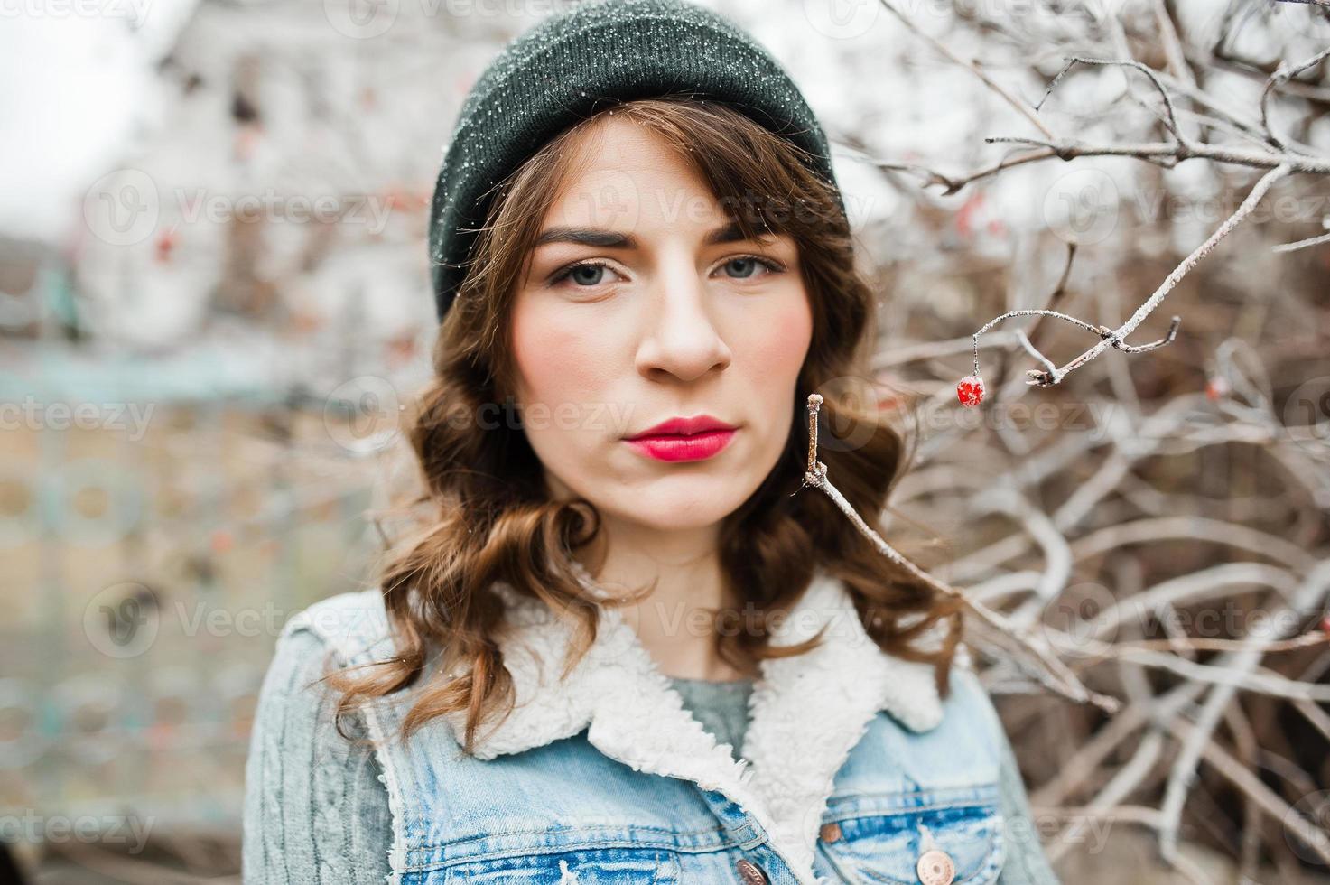 retrato de menina morena de chapéu e jaqueta jeans em arbustos congelados. foto
