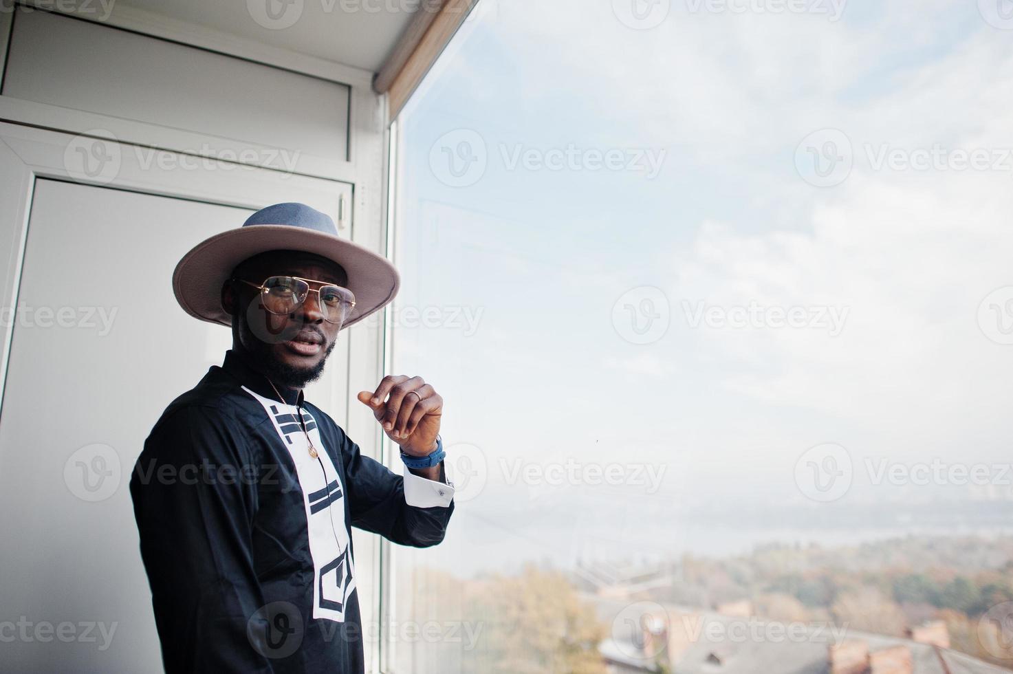 homem africano rico olhando para janela panorâmica em sua cobertura. retrato de homem negro bem sucedido no chapéu interior. foto