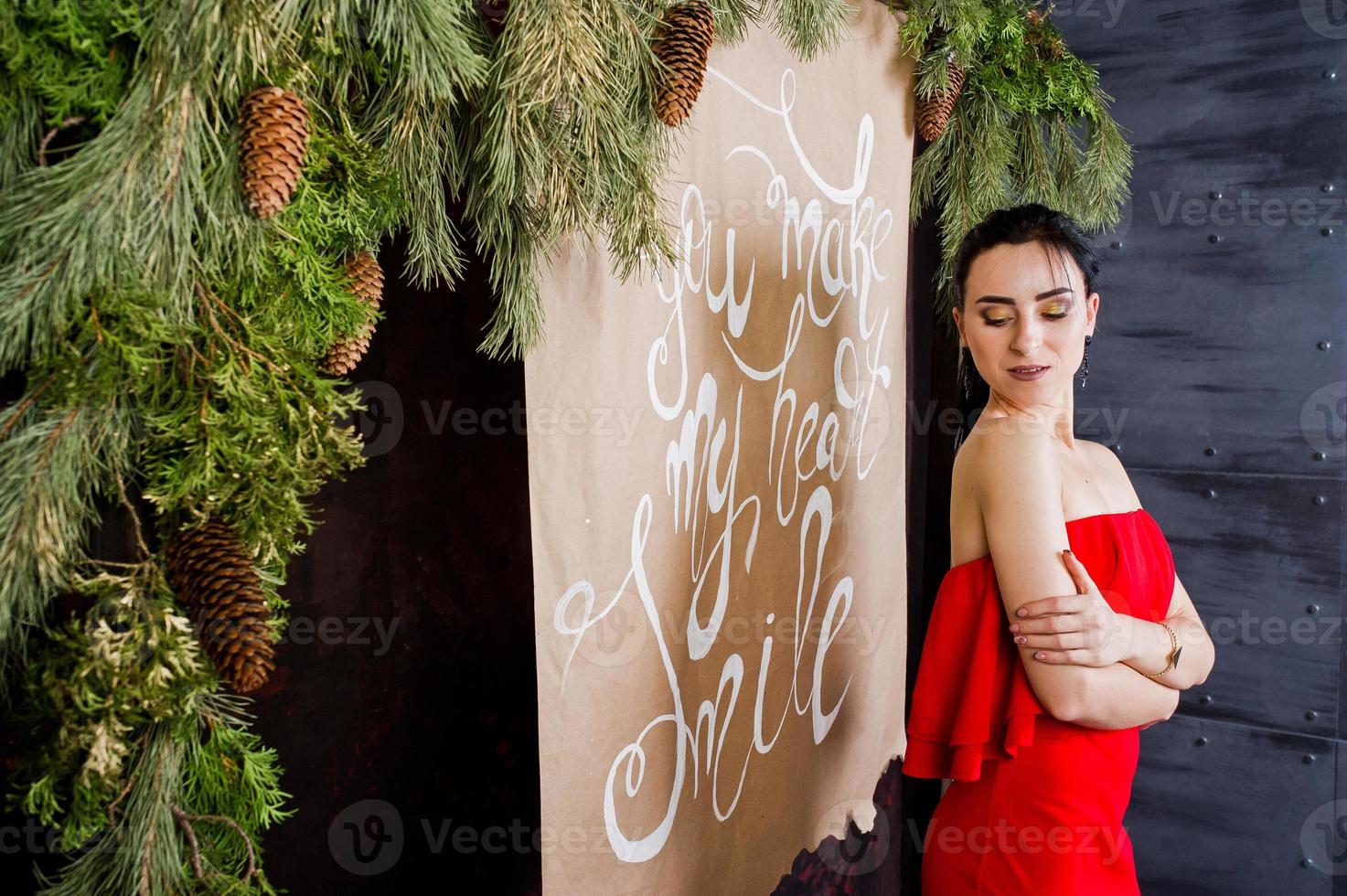 menina morena de vestido vermelho posou perto de decoração de ano novo na sala de estúdio. foto