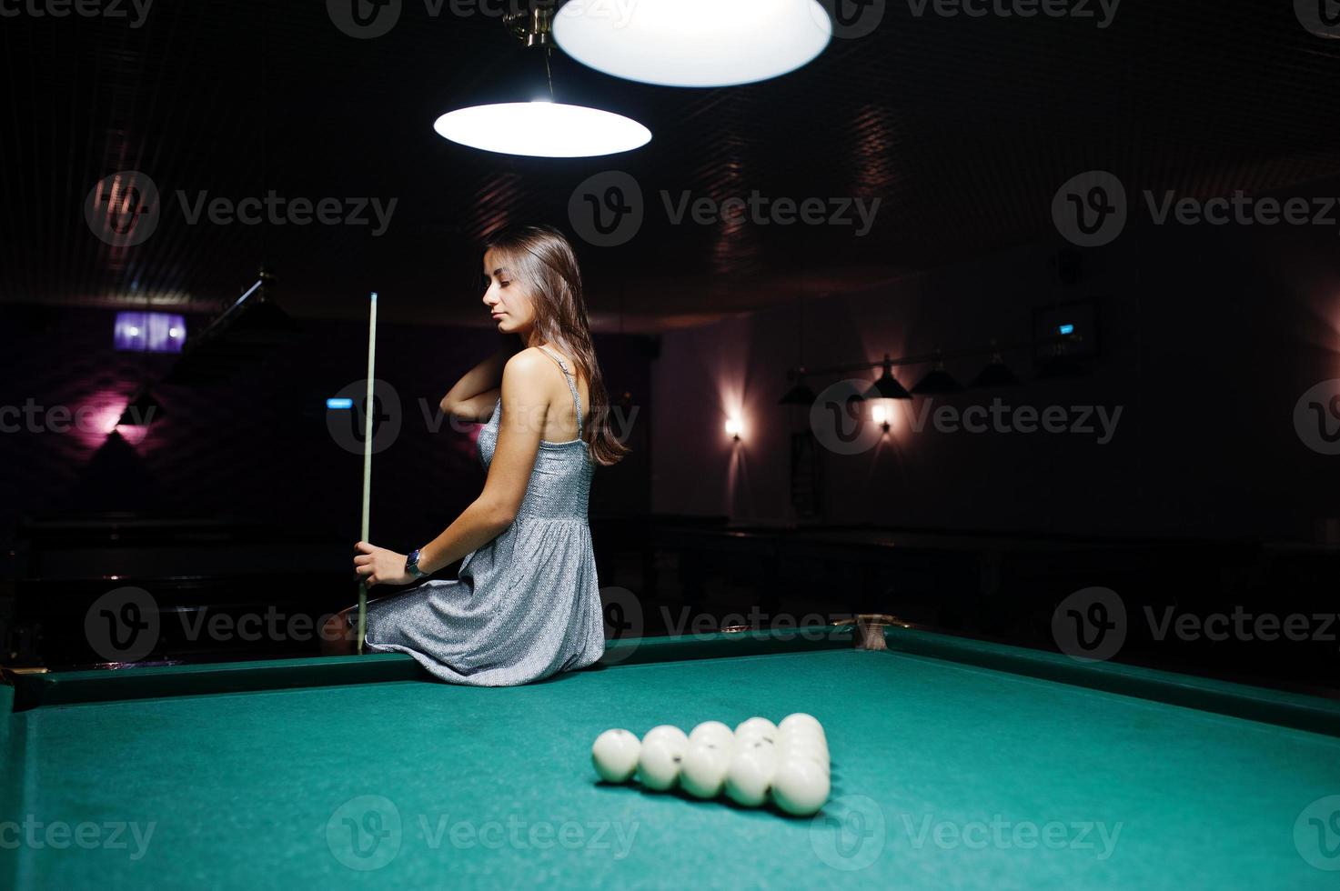 retrato de uma jovem atraente vestida sentado na mesa de bilhar e segurando um taco. foto