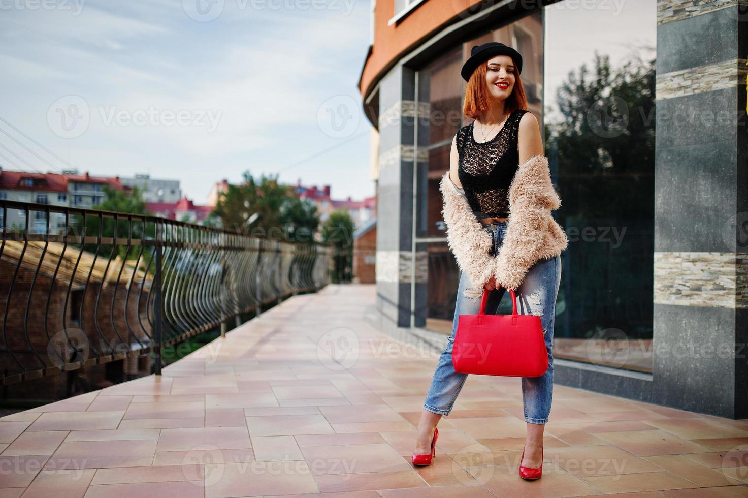 garota ruiva de chapéu com bolsa vermelha posou perto de casa moderna. foto