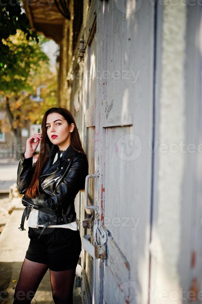 menina morena elegante usar jaqueta de couro e shorts posando na rua. foto