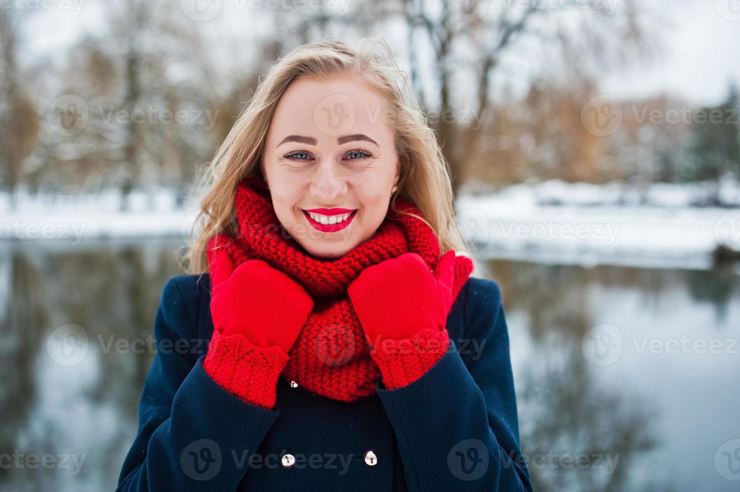 retrato de menina loira de cachecol vermelho e casaco contra lago congelado em dia de inverno. foto