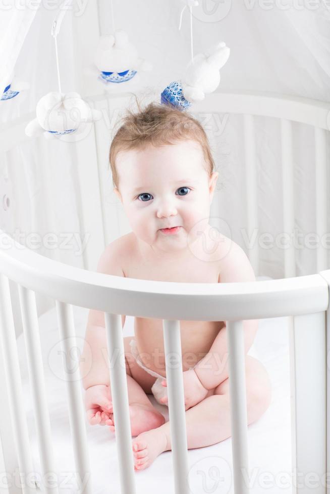 bebê muito bonito, sentado em um berço redondo branco foto