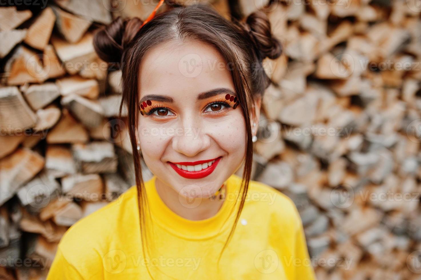 jovem garota engraçada com maquiagem brilhante, usar camisa amarela contra fundo de madeira. foto