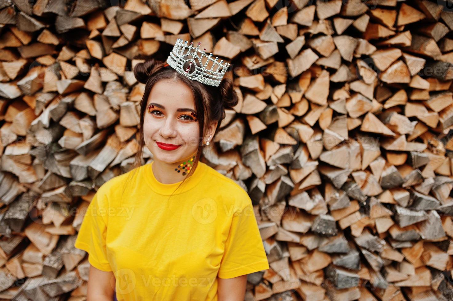 jovem garota engraçada com maquiagem brilhante, como princesa de conto de fadas, usar camisa amarela e coroa contra fundo de madeira. foto