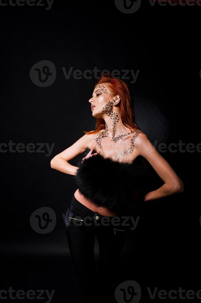 menina ruiva modelo de moda com maquiagem originalmente como predador de leopardo isolado em preto. retrato de estúdio. foto
