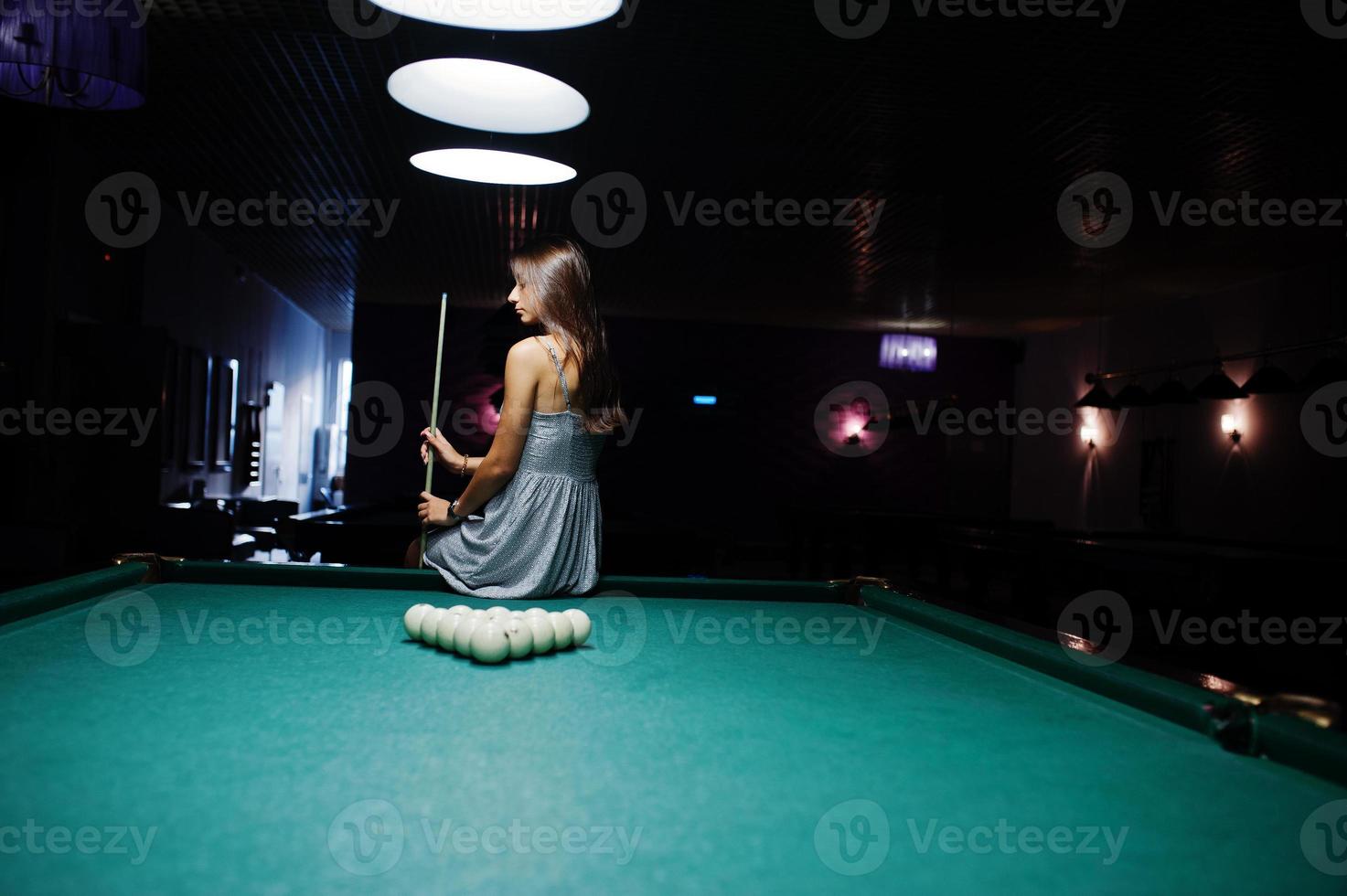 retrato de uma jovem atraente vestida sentado na mesa de bilhar e segurando um taco. foto