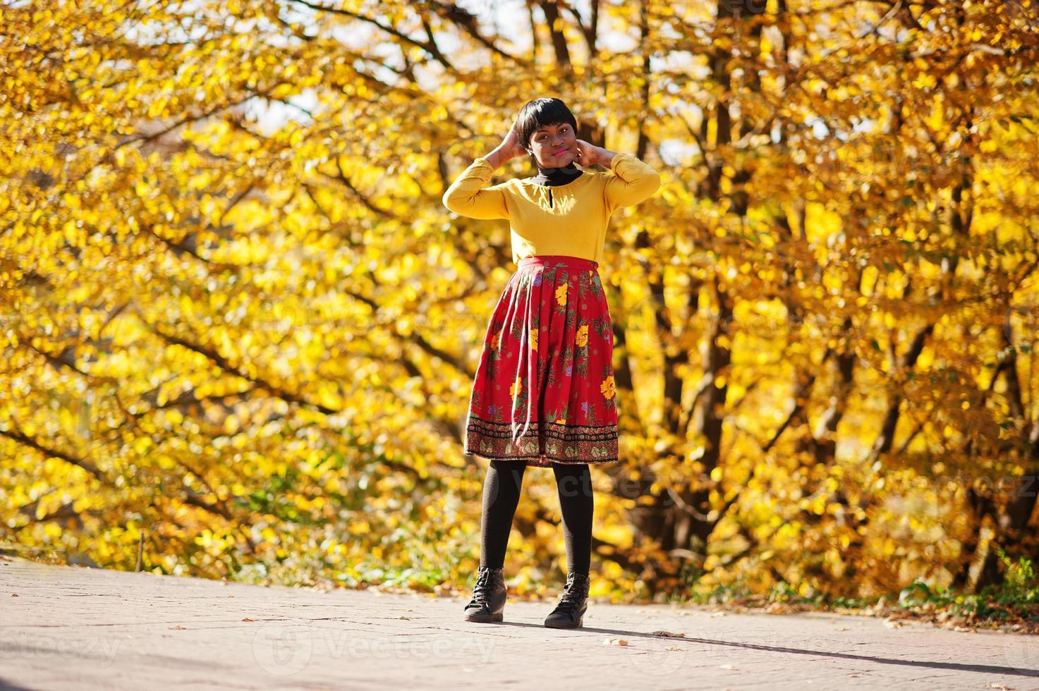 garota afro-americana no vestido amarelo e vermelho no parque outono outono dourado. foto
