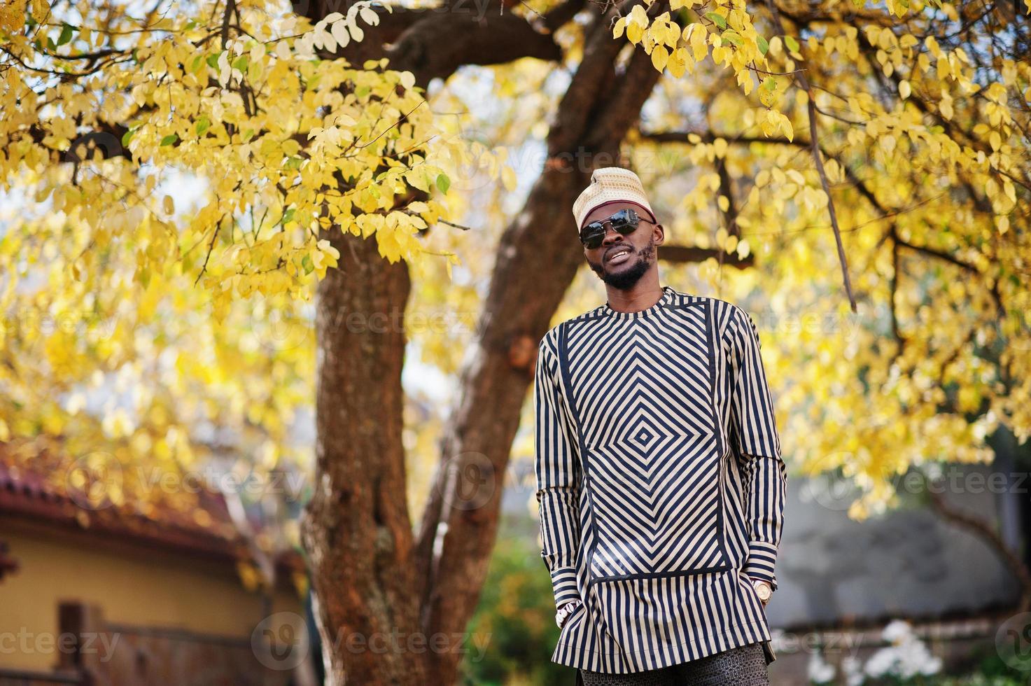 retrato de homem afro-americano elegante preto no chapéu e óculos de sol contra o fundo de outono ensolarado outono. pessoas ricas da áfrica em trajes tradicionais. foto