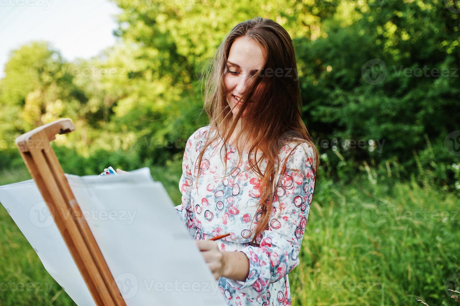 retrato de uma jovem atraente em vestido longo pintando com aquarela na natureza. foto