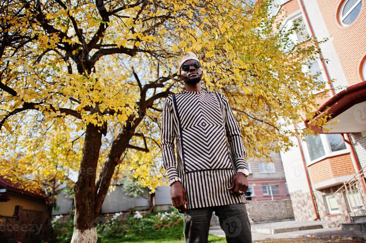 retrato de homem afro-americano elegante preto no chapéu e óculos de sol contra o fundo de outono ensolarado outono. pessoas ricas da áfrica em trajes tradicionais. foto