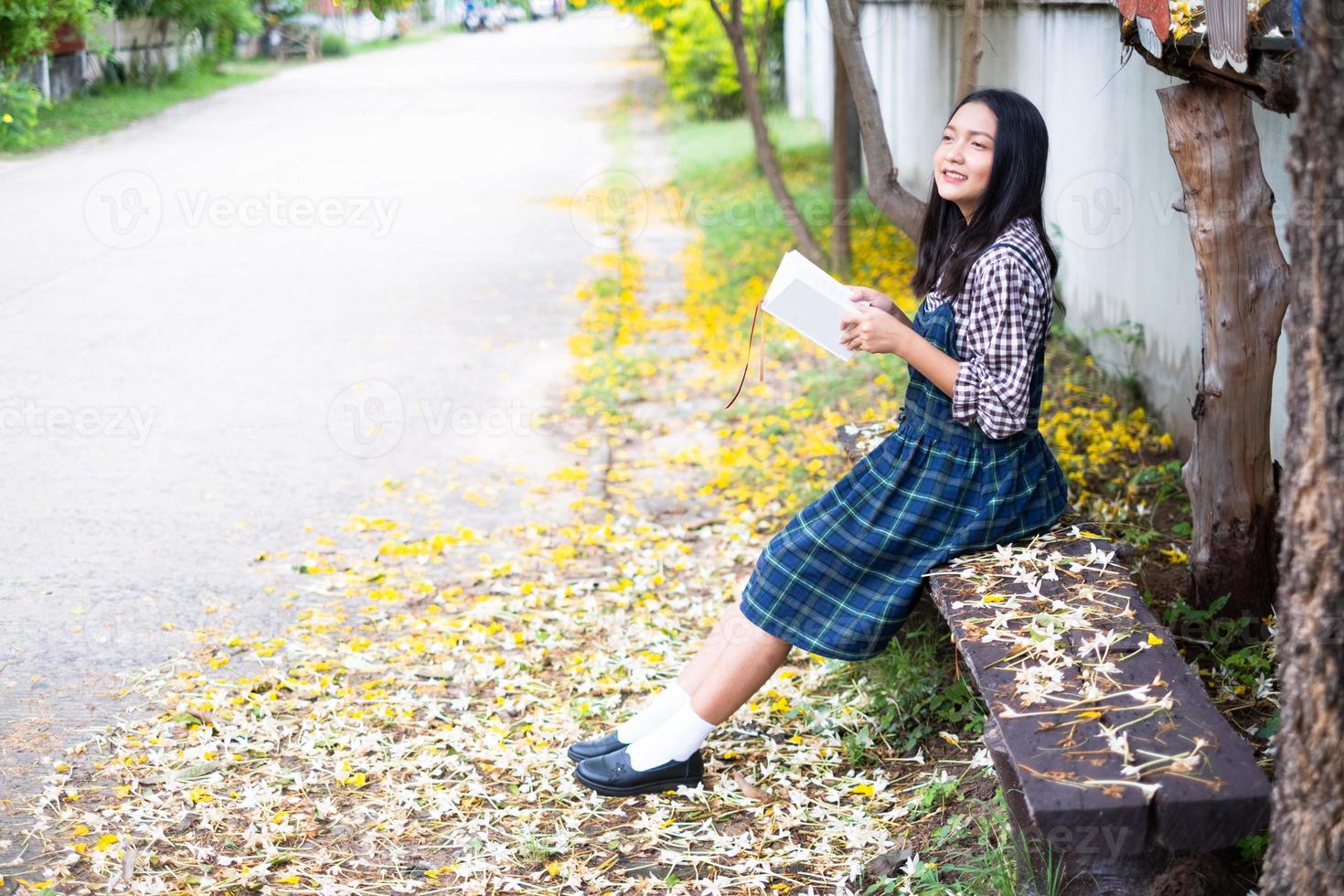 jovem sentada em um banco lendo um livro debaixo de uma bela árvore. foto