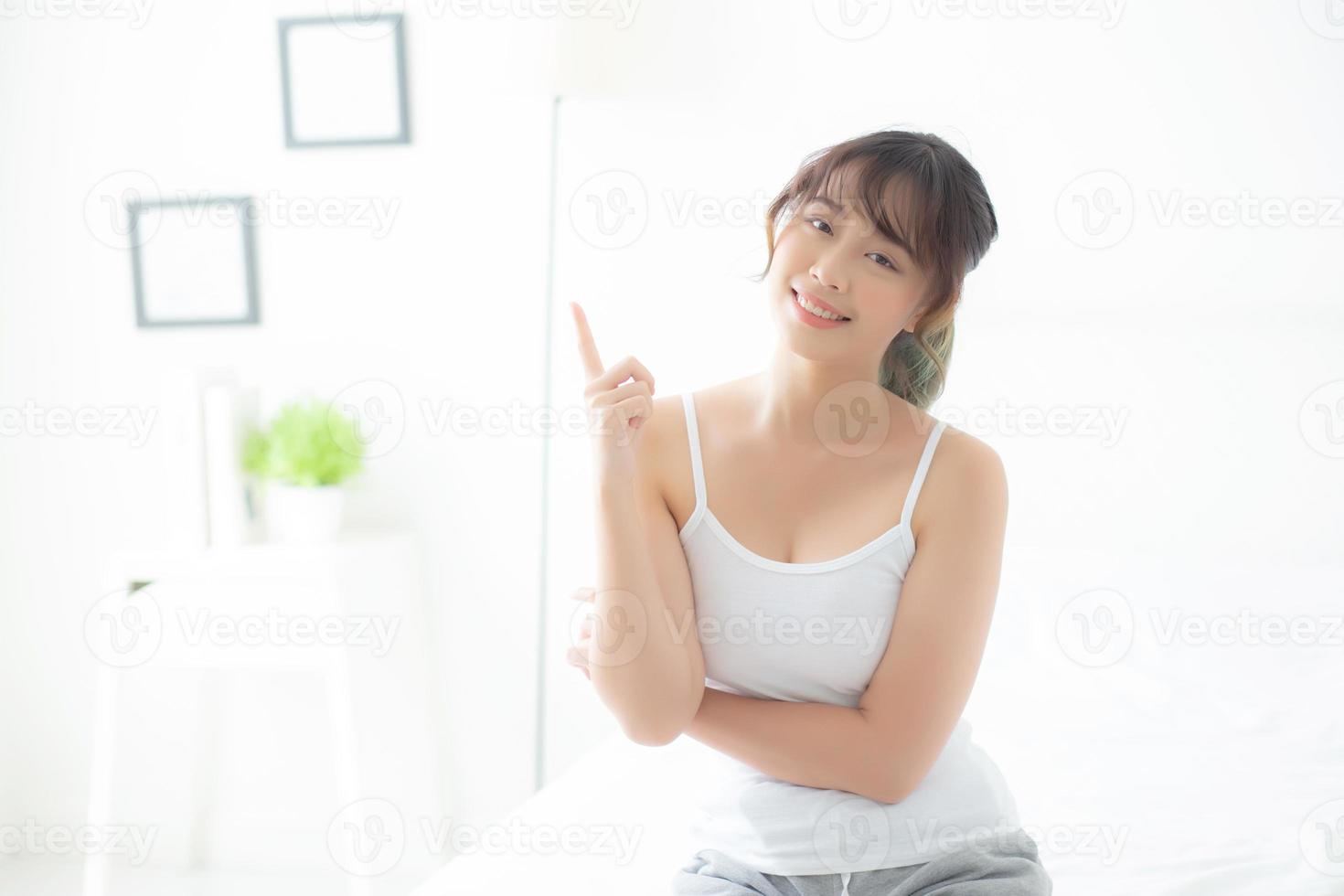 belo retrato jovem mulher asiática sorrindo saudável e bem-estar no quarto, garota de ásia de beleza tendo a ideia de apresentar e apontar algo cuidados com a pele e maquiagem cosmética, conceito de estilo de vida. foto