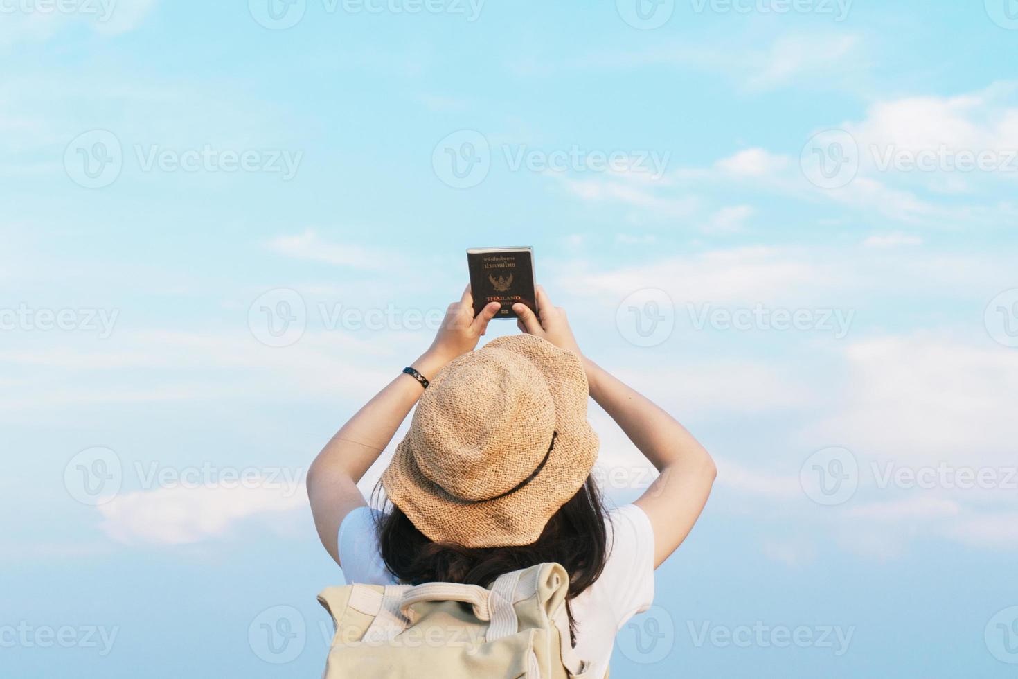 viajante de mulher com mochila segurando chapéu e passaporte da tailândia olhando para o céu azul, conceito de viagem, espaço para texto e momento atmosférico foto