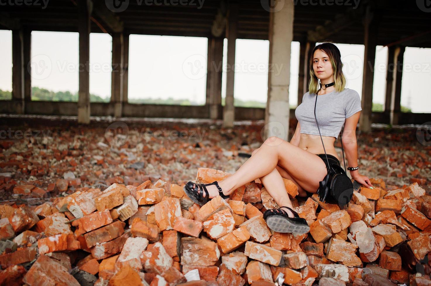 garota usa shorts na fábrica abandonada, sentado no tijolo. foto