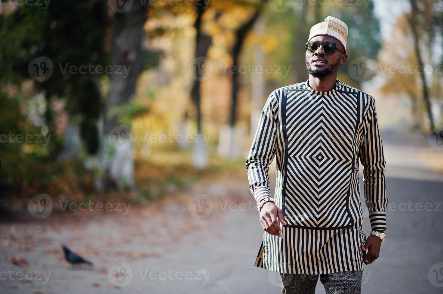 retrato de homem afro-americano elegante preto no chapéu e óculos de sol contra o fundo de outono ensolarado outono. pessoas ricas da áfrica em trajes tradicionais. foto