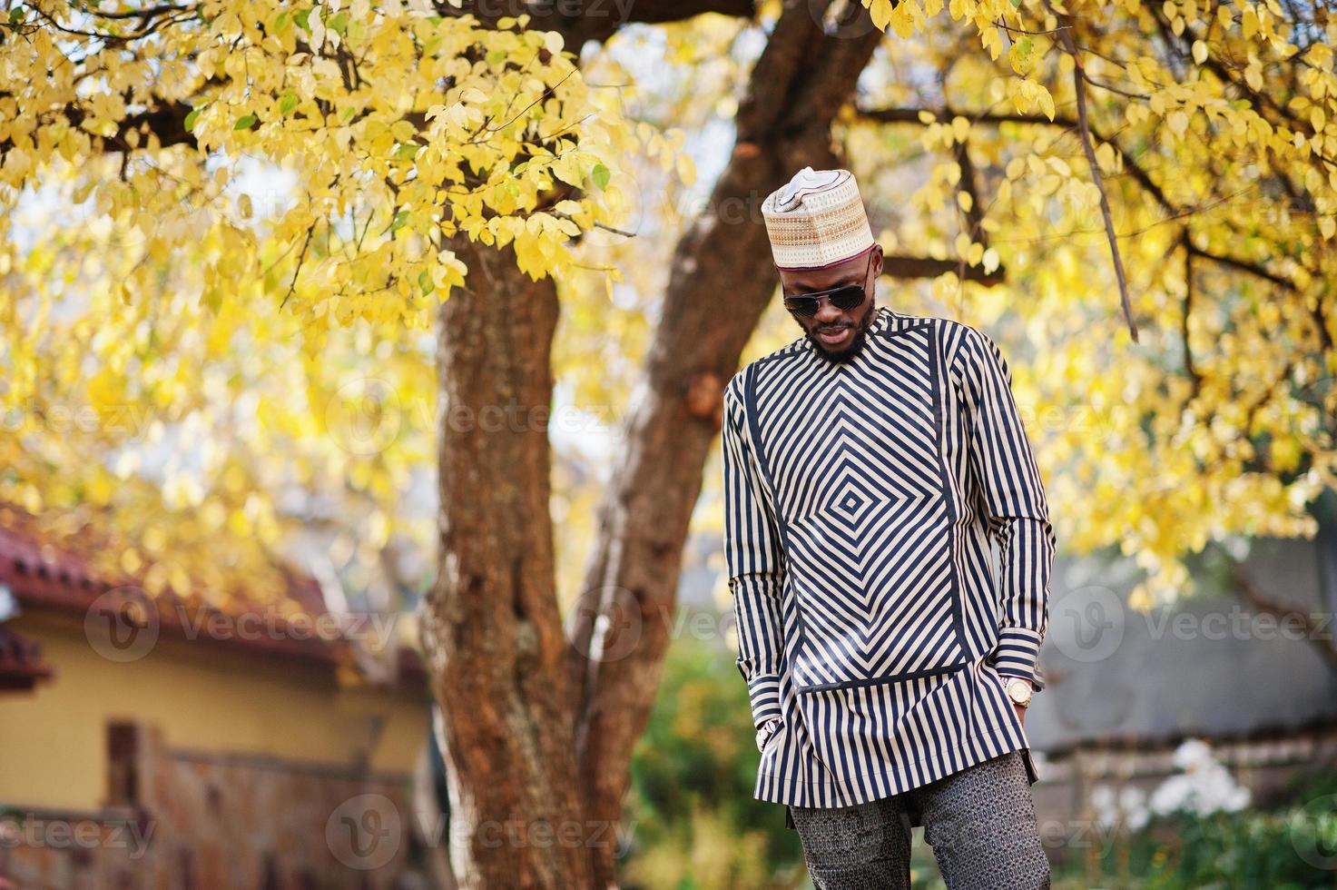 retrato de homem afro-americano elegante preto no chapéu e óculos de sol contra o fundo de outono ensolarado outono. pessoas ricas da áfrica em trajes tradicionais. foto