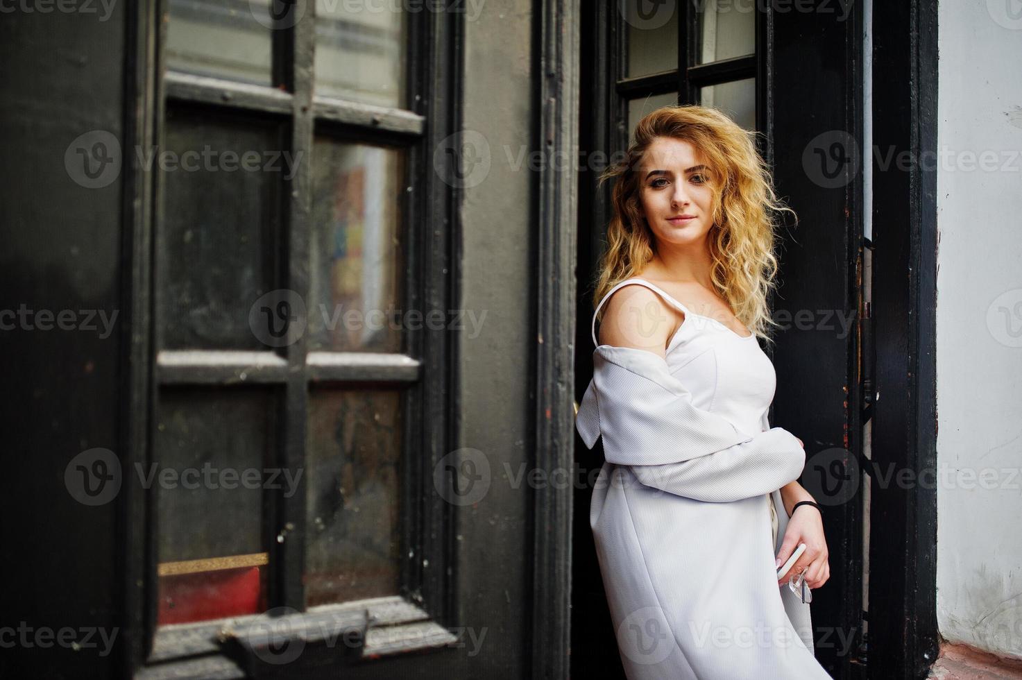 menina elegante modelo loira encaracolada usar branco posando contra a velha porta de madeira. foto