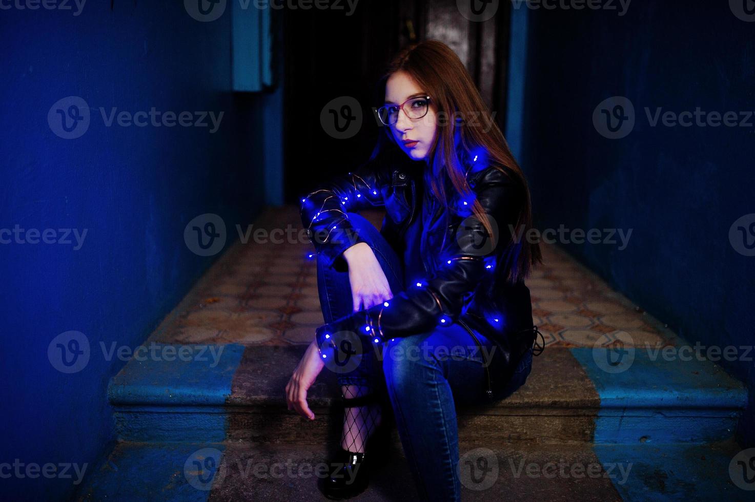 retrato noturno do modelo de menina usar óculos, jeans e jaqueta de couro, com guirlanda azul nela. foto