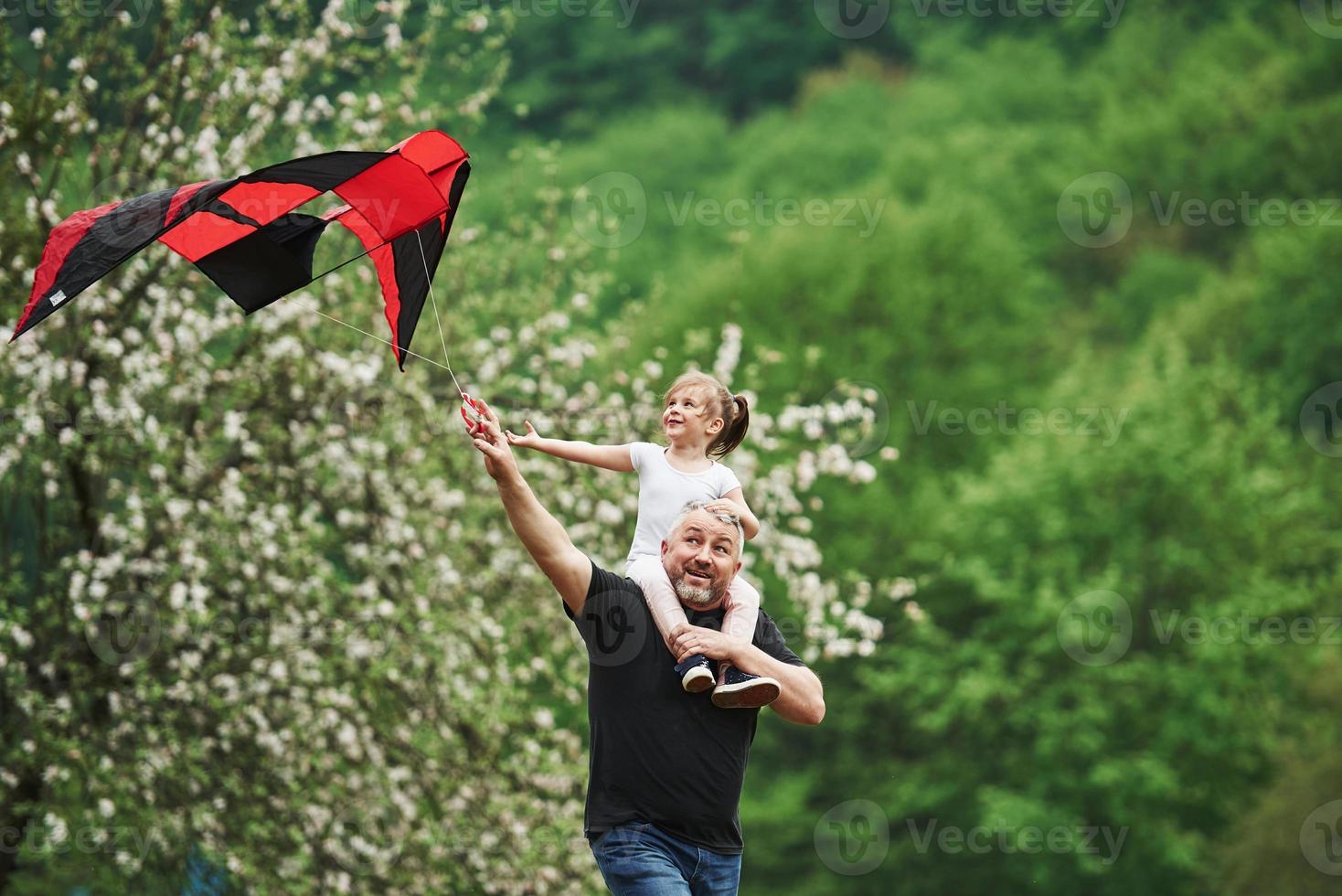 passar o fim de semana juntos. correndo com pipa vermelha. criança sentada nos ombros do homem. se divertindo foto