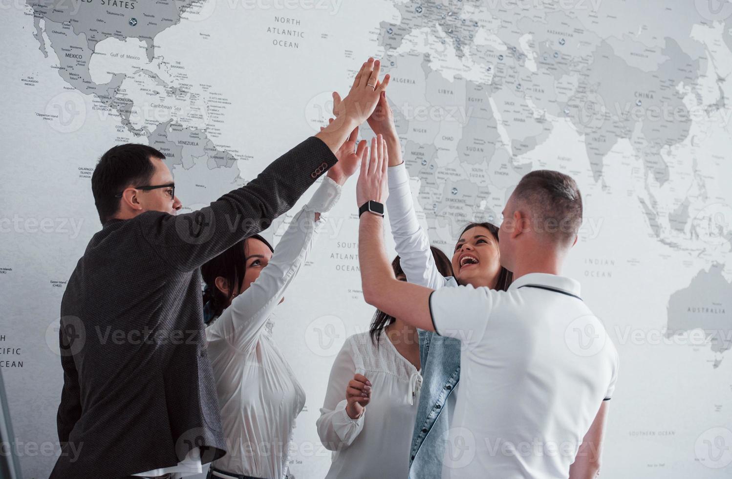 comemorando o sucesso. equipe de freelancers em pé contra a parede com mapa do mundo nele foto