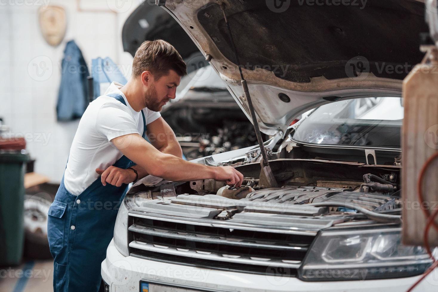 este homem sabe qual é o seu trabalho. funcionário de uniforme de cor azul trabalha no salão de automóveis foto