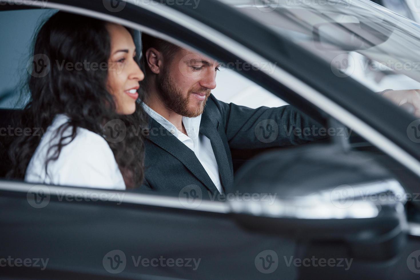 vista lateral. lindo casal bem sucedido tentando carro novo no salão de automóveis foto