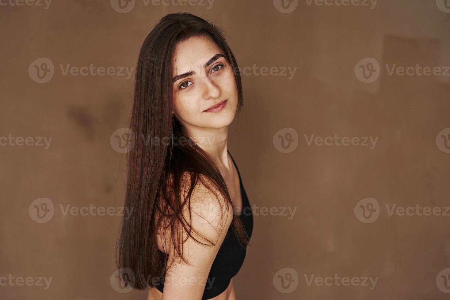 linda garota sensual. jovem mulher bonita em pé no estúdio contra fundo marrom foto