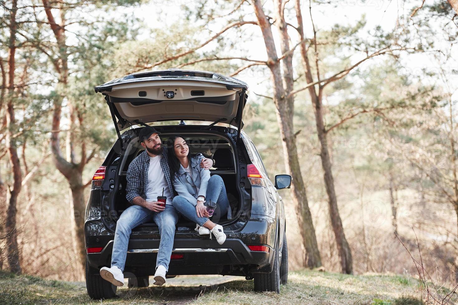 cenário rural. sentado na parte traseira do automóvel. curtindo a natureza. casal chegou à floresta em seu novo carro preto foto