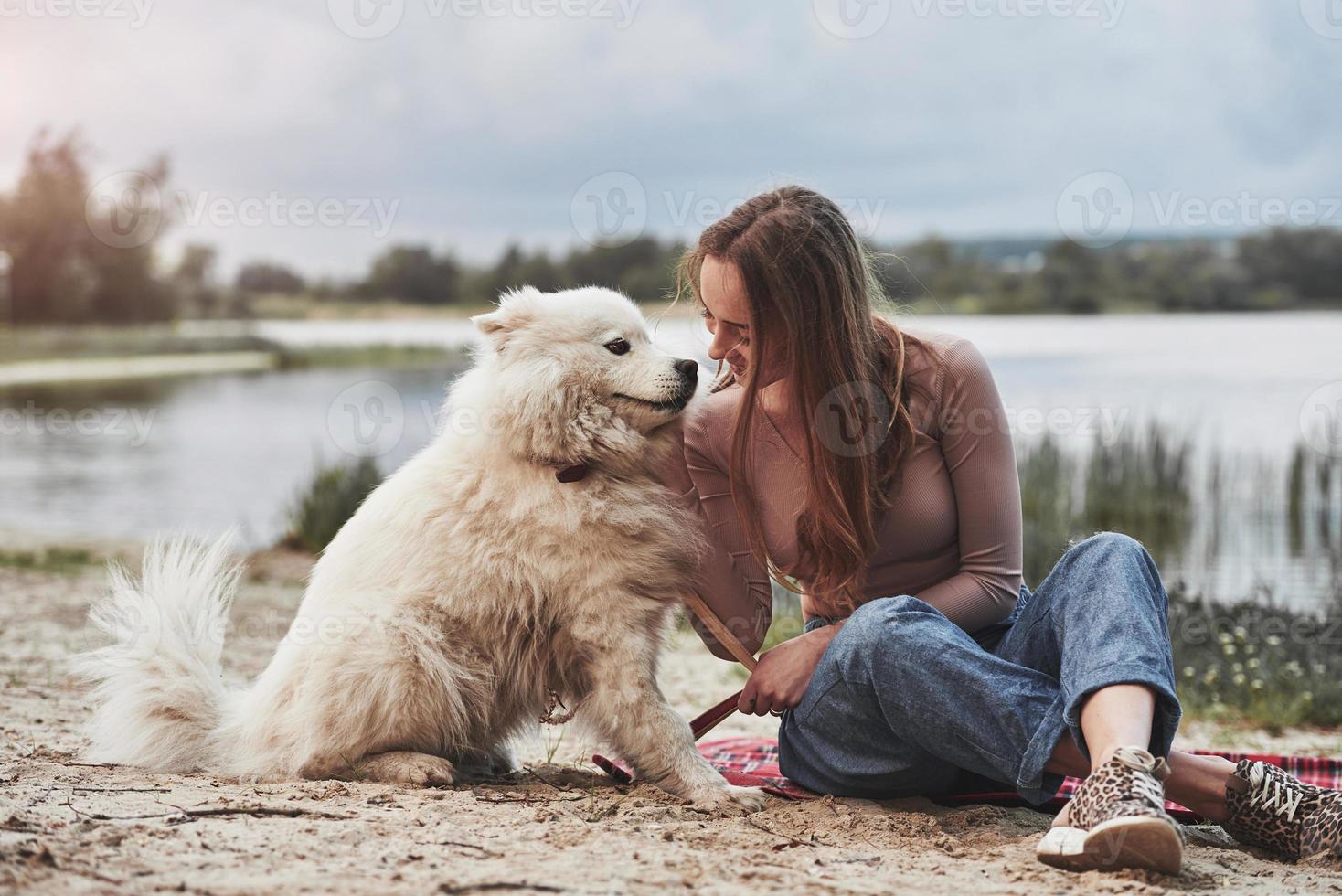 boa caminhada. menina loira com seu lindo cachorro branco se diverte muito na praia foto