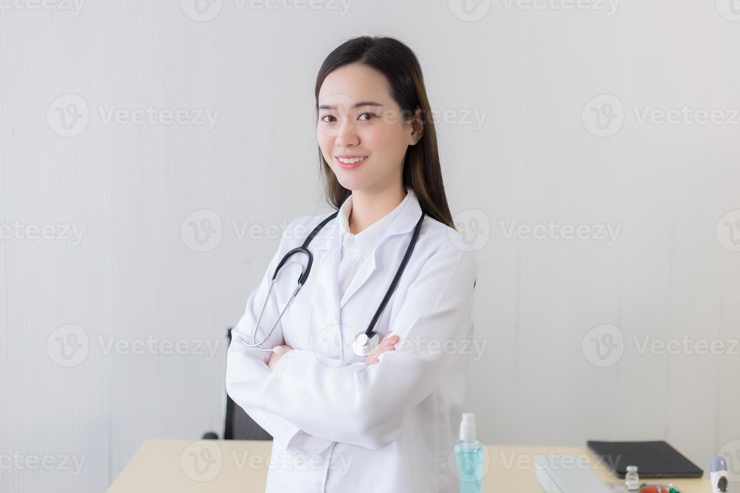 médico jovem bela mulher asiática em pé com os braços cruzados feliz e sorriso no hospital. vestindo uma túnica branca e estetoscópio foto