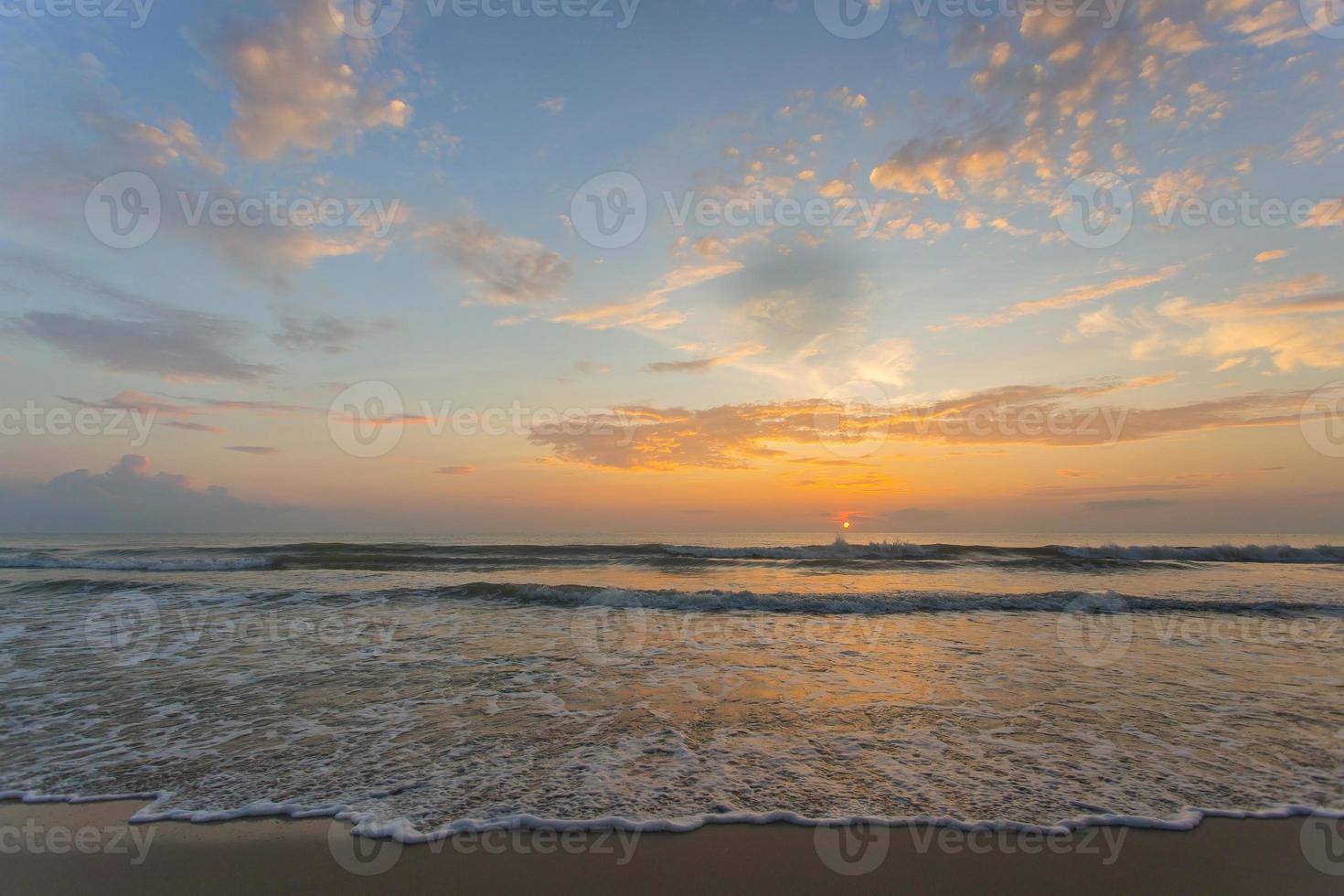 o mar está lambendo a praia de areia no pôr do sol da noite. céu azul laranja com fundo de vista para o mar. foto