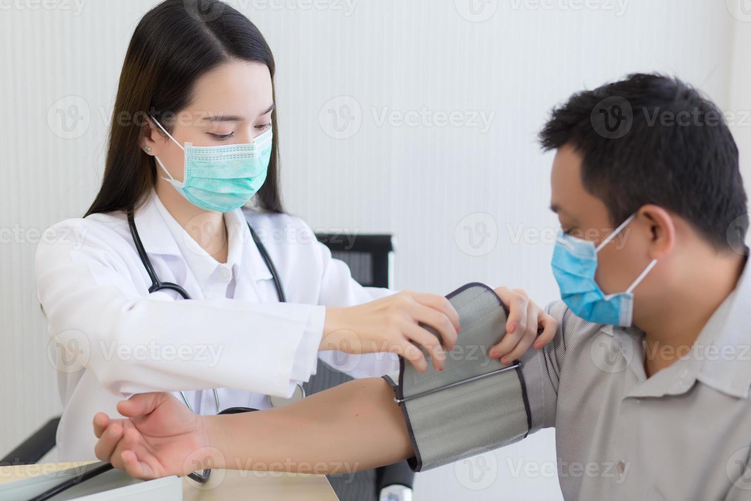 médica profissional asiática usa um medidor de pressão arterial com um paciente homem foto