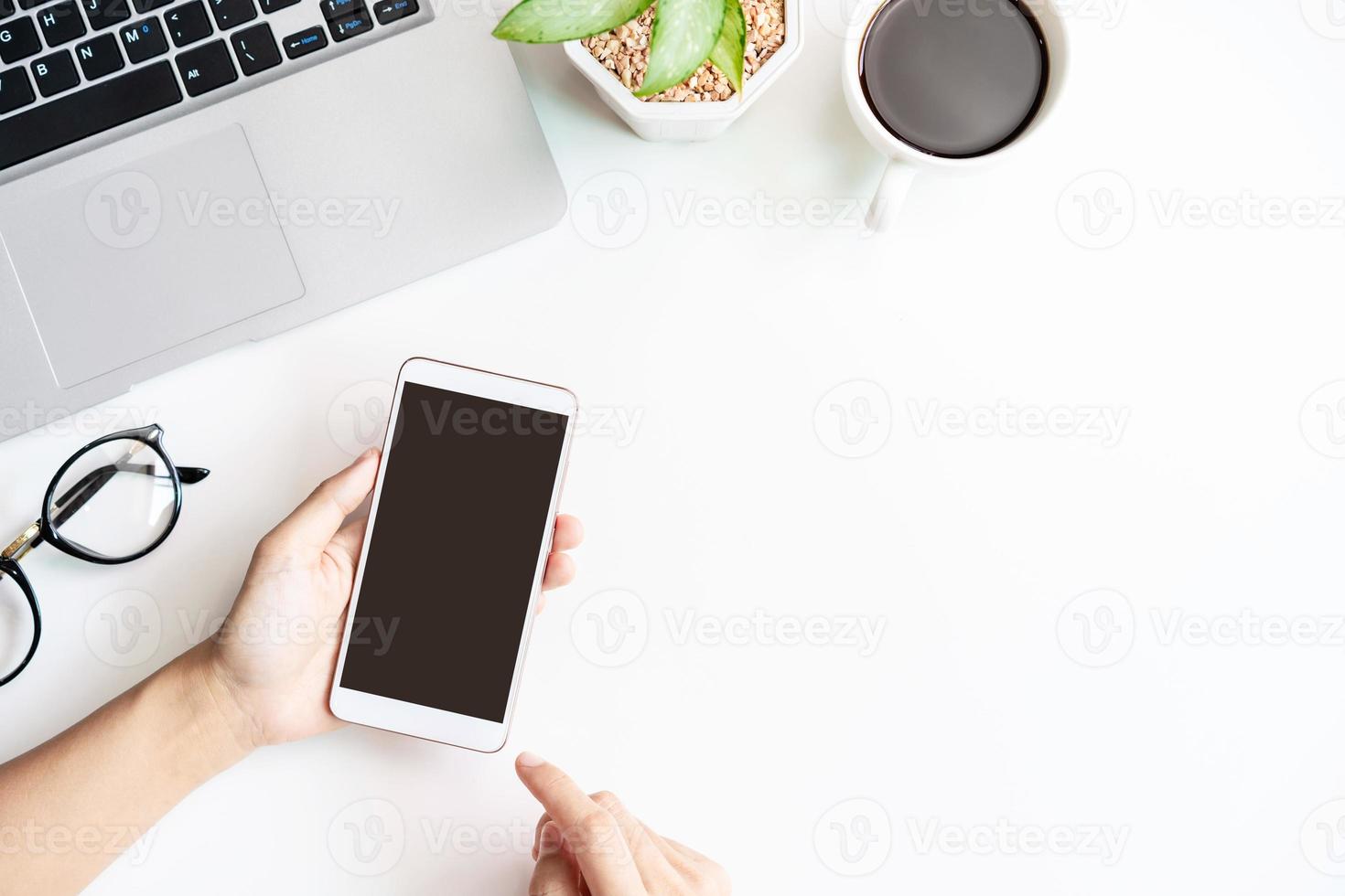 mão segurando o telefone inteligente de tela vazia no escritório de mesa de negócios com espaço de cópia, vista superior foto