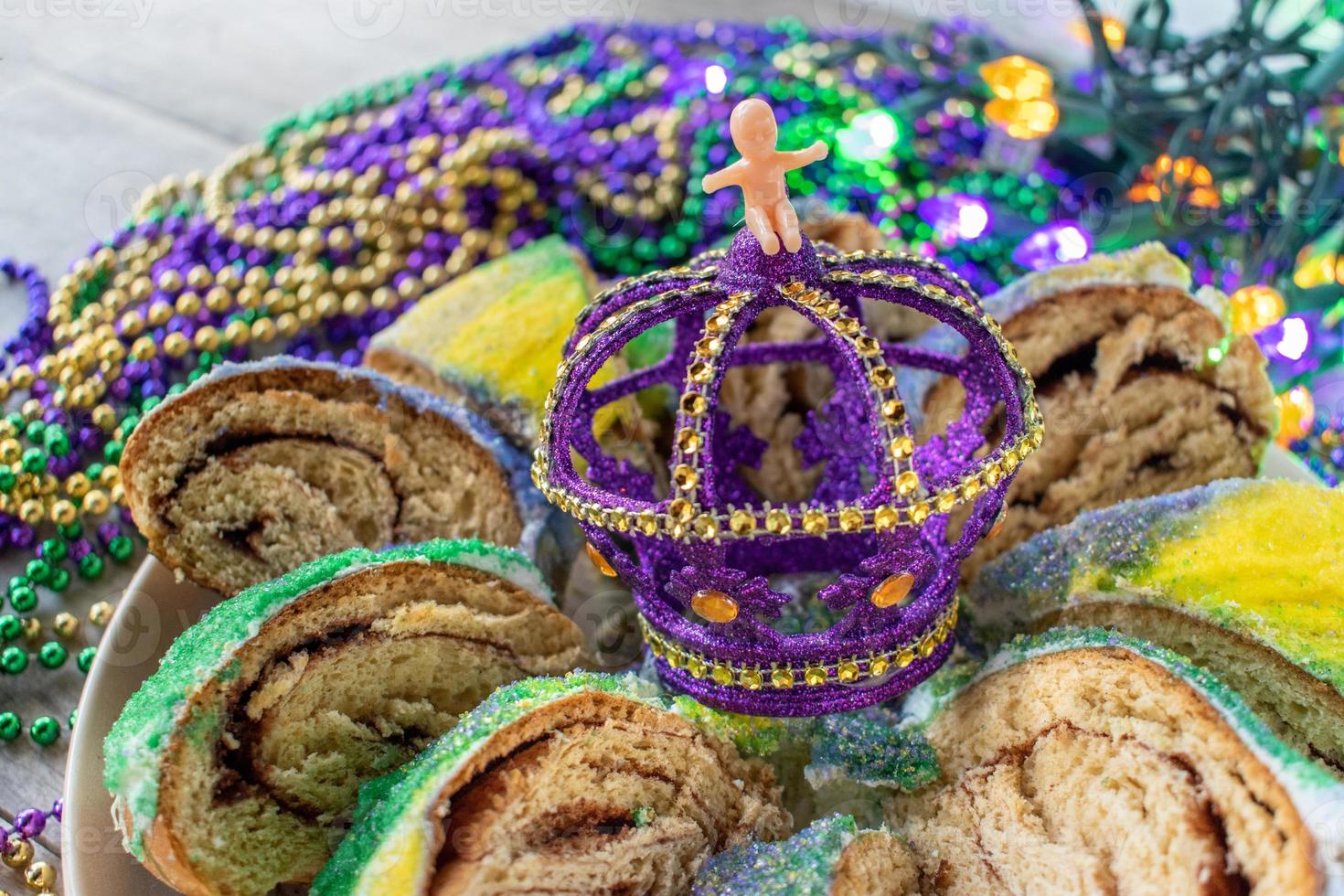 bolo de rei de carnaval fatiado com bebê cercado por contas coloridas foto